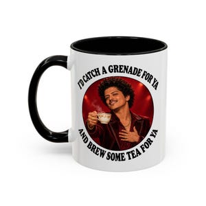 May include: A white ceramic mug with a black handle and interior rim. The front features a circular graphic of a person with curly hair in a maroon jacket holding a teacup, surrounded by the black text: I'D CATCH A GRENADE FOR YA AND BREW SOME TEA FOR YA.