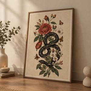Könnte beinhalten: Ein gerahmter Kunstdruck mit einer dunklen, gemusterten Schlange, die sich zwischen leuchtend roten und weißen Blumen, grünen Blättern und kleinen orangefarbenen Schmetterlingen windet. Das Bild liegt auf einem beigen, strukturierten Hintergrund.