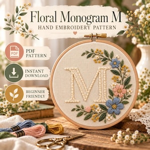 May include: A wooden embroidery hoop containing a cream-colored fabric with a stitched letter M surrounded by blue, pink, and yellow floral embroidery. The text reads Floral Monogram M Hand Embroidery Pattern, PDF Pattern, Instant Download, and Beginner Friendly.
