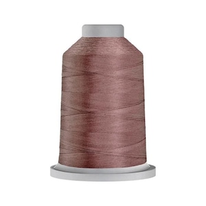 May include: A spool of dusty rose colored sewing thread featuring a smooth, slightly metallic sheen. The thread is wound tightly around a cylindrical core with a flat, light gray plastic base and a matching light gray top cap.