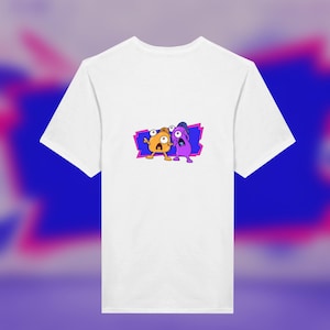 May include: A white short-sleeved t-shirt featuring a central graphic of two cartoon characters, one orange and one purple, with wide eyes and surprised expressions, set against a jagged blue and pink rectangular background shape.