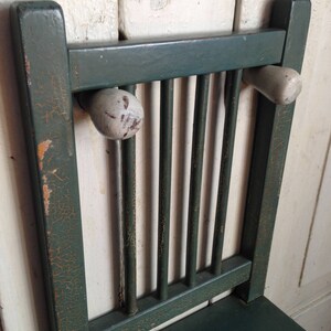Puede incluir: Una silla de madera verde con un acabado desgastado y pomos de madera blancos en el respaldo.
