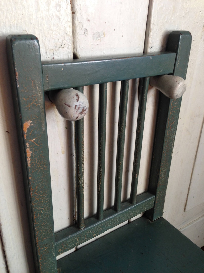 Puede incluir: Una silla de madera verde con un acabado desgastado y pomos de madera blancos en el respaldo.