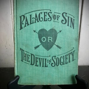 May include: A vintage green book with the title "Palaces of Sin or The Devil in Society" in black lettering. The cover features a heart with arrows and the word "OR" inside.