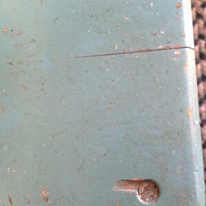 Puede incluir: Primer plano de una superficie de madera azul claro con un peque&ntilde;o tornillo de metal marr&oacute;n oscuro en la esquina inferior derecha. La superficie est&aacute; desgastada y tiene algunos ara&ntilde;azos.