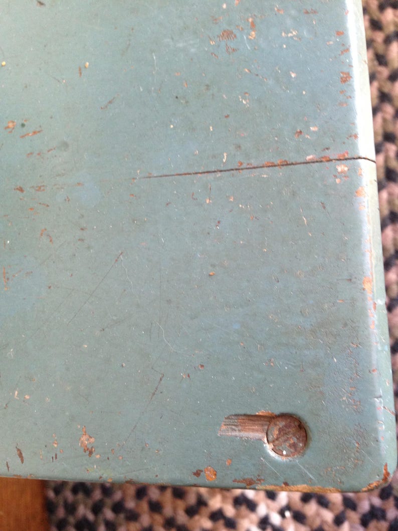 Puede incluir: Primer plano de una superficie de madera azul claro con un peque&ntilde;o tornillo de metal marr&oacute;n oscuro en la esquina inferior derecha. La superficie est&aacute; desgastada y tiene algunos ara&ntilde;azos.