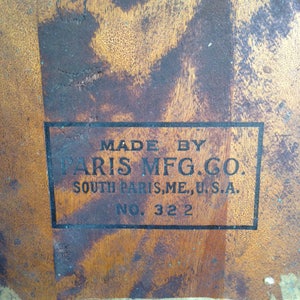 Puede incluir: Primer plano de una superficie de madera con una etiqueta negra que dice "Made by Paris Mfg. Co. South Paris, ME, U.S.A. No. 322".
