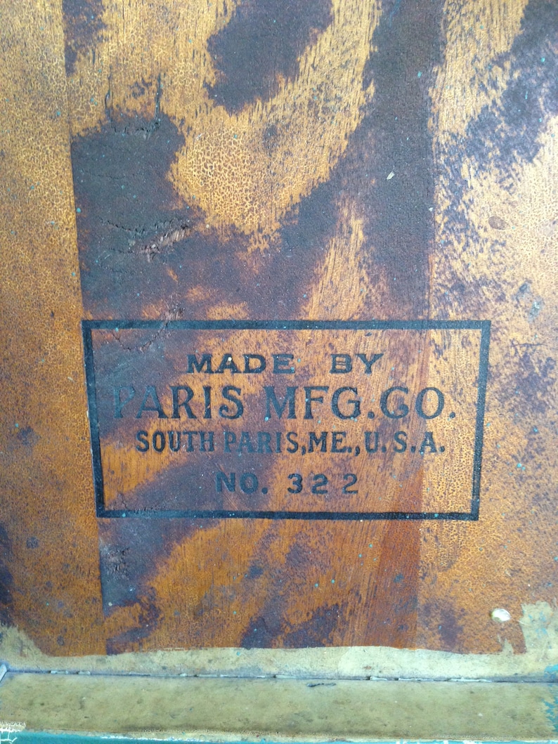 Puede incluir: Primer plano de una superficie de madera con una etiqueta negra que dice "Made by Paris Mfg. Co. South Paris, ME, U.S.A. No. 322".