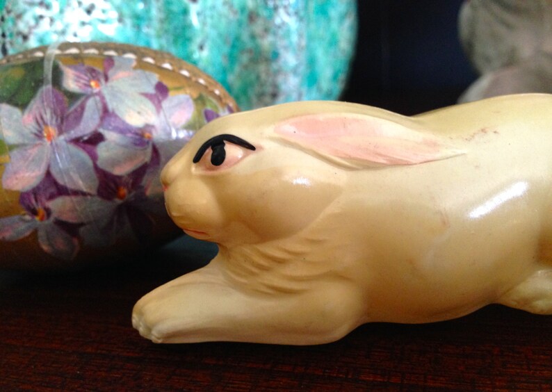 May include: A white ceramic rabbit figurine with a pink ear and black eye. The rabbit is lying on its side with its head turned to the side.