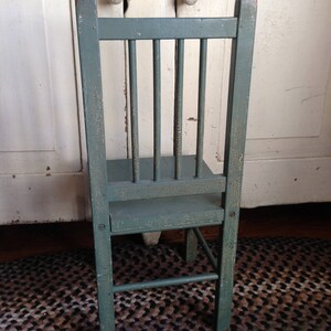 Puede incluir: Una peque&ntilde;a silla de madera verde con respaldo de listones y un dise&ntilde;o sencillo. La silla es de estilo vintage y desgastado.