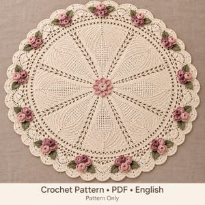May include: A round, cream-colored crochet doily featuring a central pink flower and radiating fan-like patterns. The scalloped border is decorated with small clusters of pink roses and green leaves. Text at the bottom reads: Crochet Pattern • PDF • English • Pattern Only.