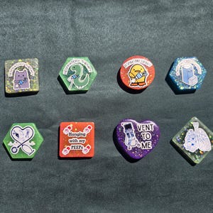 May include: Eight resin badges in various shapes including square, hexagon, circle, heart, and diamond. Each piece features glitter and a unique graphic related to respiratory therapy, including illustrations of lungs, inhalers, and cartoon characters.