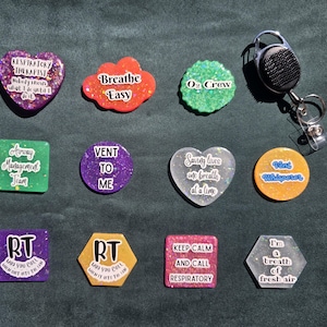 May include: A collection of eleven colorful resin badge reels and pins featuring various shapes and medical-themed text including Respiratory Therapist, Breathe Easy, O2 Crew, Airway Management Team, Vent To Me, Saving lives one breath at a time, Vent Whisperer, RT, Keep calm and call respiratory, and I'm a breath of fresh air.