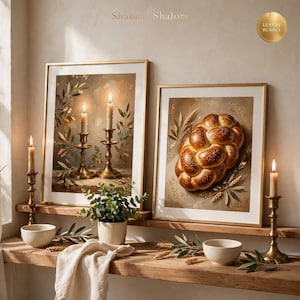 May include: Two framed wall art prints displayed on wooden shelves. One print features two lit candles in brass holders surrounded by olive branches. The other print shows a braided challah bread loaf. The text Shabbat Shalom appears above.