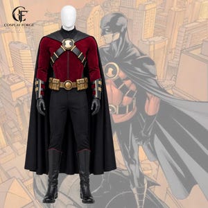 May include: A superhero costume on a mannequin featuring a deep red velvet long-sleeve top, black trousers, a black cape, and black gloves. The outfit includes a gold-toned chest emblem, a utility belt with pouches, and black knee-high boots.