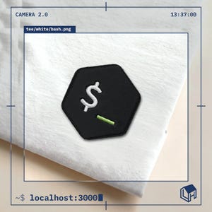 Peut inclure: Un t-shirt blanc orné d'un écusson brodé hexagonal noir. L'écusson présente un symbole dollar blanc et une ligne horizontale vert clair, rappelant une interface de ligne de commande sur un fond sombre.