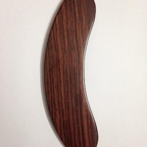 May include: A curved, crescent-shaped wooden tool with a smooth, polished finish. The object features a deep reddish-brown colour with a prominent, dark vertical wood grain pattern running along its entire length, tapering to rounded points.