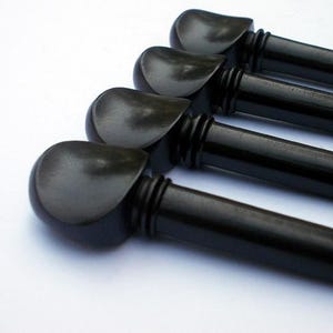 May include: A set of four black violin tuning pegs arranged in a parallel row. Each peg features a smooth, rounded head with a curved indentation and a cylindrical shaft with two distinct decorative rings near the base of the head.