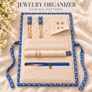 May include: A fabric jewelry organizer sewing pattern featuring a cream-colored quilted interior with blue and white floral trim. It includes two necklace tabs, a ring holder, a zippered pocket, and a small flap for earrings with the text JEWELRY ORGANIZER SEWING PATTERN.