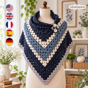 Könnte beinhalten: Ein gehäkeltes Schultertuch mit V-förmigem Design und abwechselnden Streifen aus marineblauem, hellblauem und cremefarbenem Garn. Das Kleidungsstück wird am Halsausschnitt mit zwei hellen Holzknöpfen geschlossen. Der Text Talhadesignhub ist sichtbar.