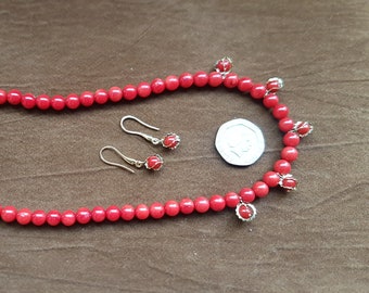 May include: A red coral necklace and matching earrings. The necklace is made of small, round beads and has a gold clasp. The earrings are also made of red coral and have a gold wire design.
