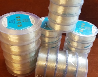 Op de afbeelding: Meerdere spoelen met heldere elastische draad, elk verpakt in plastic en gelabeld met de tekst "Elastic String 0.8mm 100M".
