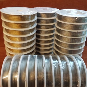 May include: Close-up of spools of gold and silver coloured thread. The thread is wound around white plastic spools and is wrapped in clear plastic.