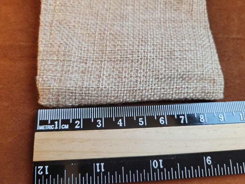 May include: Close-up of a beige fabric with a woven texture. A ruler is placed below the fabric, showing measurements in inches and centimeters.