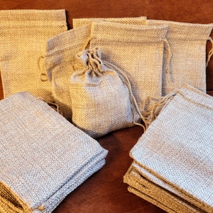 May include: A pile of small, natural burlap drawstring bags. The bags are made of a woven fabric and have a natural, rustic look. They are perfect for packaging small gifts or favors.