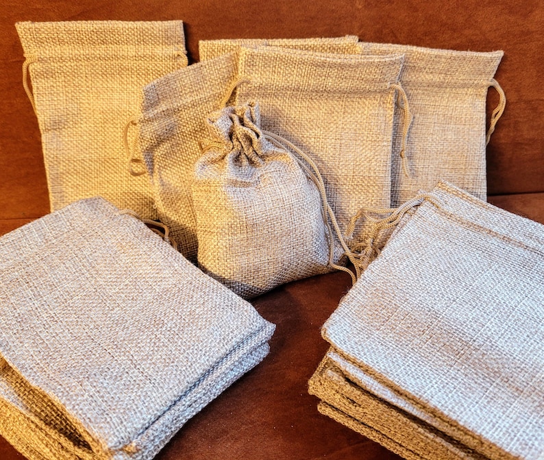 May include: A pile of small, natural burlap drawstring bags. The bags are made of a woven fabric and have a natural, rustic look. They are perfect for packaging small gifts or favors.