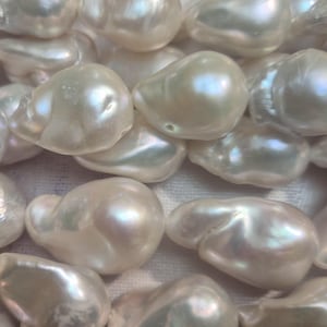 Puede incluir: Primer plano de una colecci&oacute;n de perlas lustrosas de forma irregular. Las perlas tienen un color blanco cremoso con reflejos iridiscentes, que reflejan la luz. Las perlas est&aacute;n agrupadas, mostrando sus formas org&aacute;nicas &uacute;nicas.