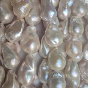 Puede incluir: Primer plano de una colecci&oacute;n de perlas barrocas blancas. Cada perla tiene una forma irregular &uacute;nica y una superficie lisa e iridiscente. Las perlas reflejan la luz, mostrando un brillo nacarado suave. Est&eacute;tica natural y elegante.