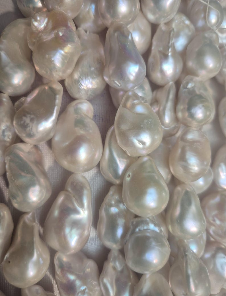 Puede incluir: Primer plano de una colecci&oacute;n de perlas barrocas blancas. Cada perla tiene una forma irregular &uacute;nica y una superficie lisa e iridiscente. Las perlas reflejan la luz, mostrando un brillo nacarado suave. Est&eacute;tica natural y elegante.
