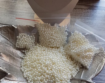 May include: A silver leaf-shaped dish filled with white pearl beads. There are three smaller bags of beads in the background.