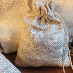 May include: A group of small, natural burlap drawstring bags. The bags are made of a woven fabric and have a natural, rustic look.