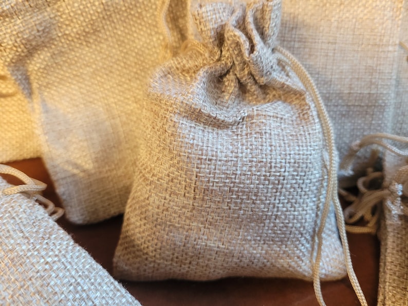 May include: A group of small, natural burlap drawstring bags. The bags are made of a woven fabric and have a natural, rustic look.