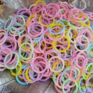 Puede incluir: Un montón grande de anillos de plástico de colores, en tonos de rosa, amarillo, azul y verde. Los anillos son todos del mismo tamaño y forma, y están dispuestos en un patrón aleatorio.