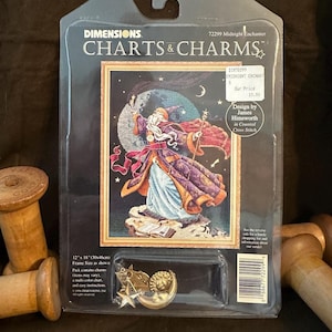 May include: A Dimensions Charts & Charms Midnight Enchanter counted cross stitch kit in original packaging. The package features an illustration of a wizard with a staff and book, plus metal star and moon charms. It measures 12 inches by 18 inches.