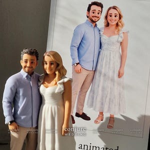 May include: A custom 3D figurine of a couple standing next to a printed photograph of the same pair. The figurine depicts a person in a light blue button-down shirt and tan pants, and a person in a white dress with ruffled sleeves.