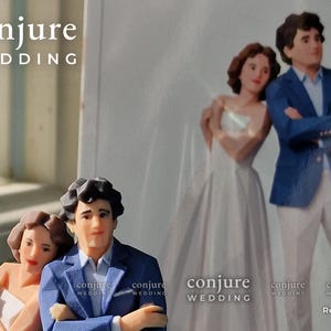 May include: A 3D printed figurine of a couple standing next to a printed photograph of the same couple. The figurine features a person in a blue blazer and white shirt with arms crossed, and a person in a white strapless dress. Text reads conjure WEDDING.