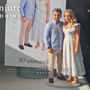 May include: A 3D printed figurine of a couple standing side by side on a circular base. The figure on the left wears a light blue button-down shirt and tan pants. The figure on the right wears a white midi dress with ruffled sleeves.