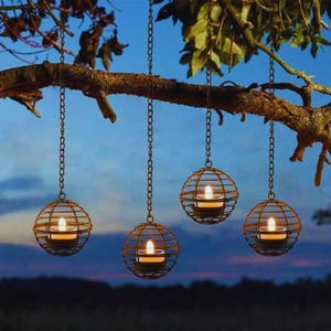 Peut inclure: Quatre lanternes sphériques en fil métallique suspendues à une branche d'arbre par des chaînes. Chaque structure en forme de cage brun foncé contient une petite bougie chauffe-plat blanche allumée. Les lanternes sont suspendues à différentes hauteurs.