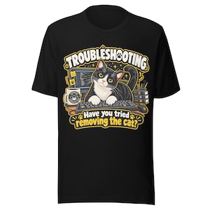 Può includere: Una t-shirt nera con la grafica di un gatto tuxedo seduto davanti a una tastiera di computer. Il testo recita TROUBLESHOOTING e Have you tried removing the cat? Il design include una tazza da caffè, un monitor di computer e dei libri.