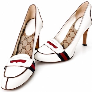 Peut inclure: Une paire d'escarpins à talons hauts en cuir blanc avec un devant style mocassin orné d'une bande rayée rouge et bleu marine. La doublure intérieure présente un motif monogramme beige et marron, et les talons sont finis avec un liseré marron.