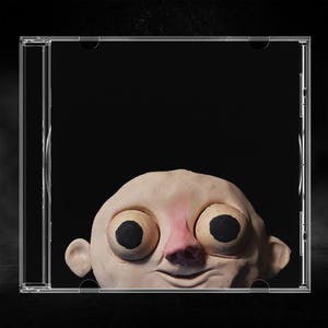 May include: A clear plastic CD jewel case containing a sculpted clay head with a pale beige complexion, a prominent pink nose, and two large, round, bulging eyes with solid black pupils, all set against a stark, solid black background.