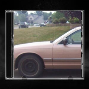 May include: A light pink sedan is shown from the side profile, featuring a dark wheel, a side mirror, and a window frame. The car is positioned in front of a grassy area with a house and other vehicles visible in the background.
