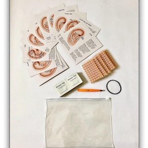 May include: An ear acupuncture kit containing a set of instructional cards with ear diagrams, a sheet of small adhesive ear seeds, two alcohol pads, an orange plastic tweezer, a black elastic band, and a clear plastic zippered storage pouch.