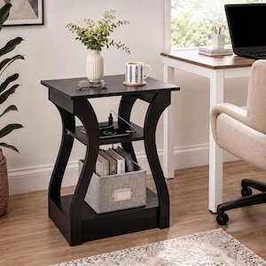 May include: A black wooden end table with a square top, a middle shelf featuring a built-in power strip with charging ports, and a bottom shelf holding a grey fabric storage bin. The table has curved side supports and a dark wood grain finish.