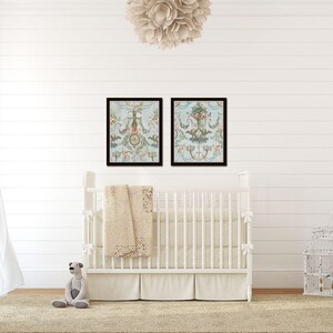 May include: A white crib with a white and beige blanket in a nursery with white walls and a white dresser. Two framed prints with floral designs hang above the crib.