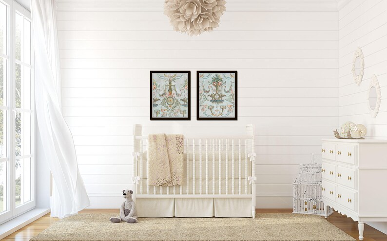 May include: A white crib with a white and beige blanket in a nursery with white walls and a white dresser. Two framed prints with floral designs hang above the crib.